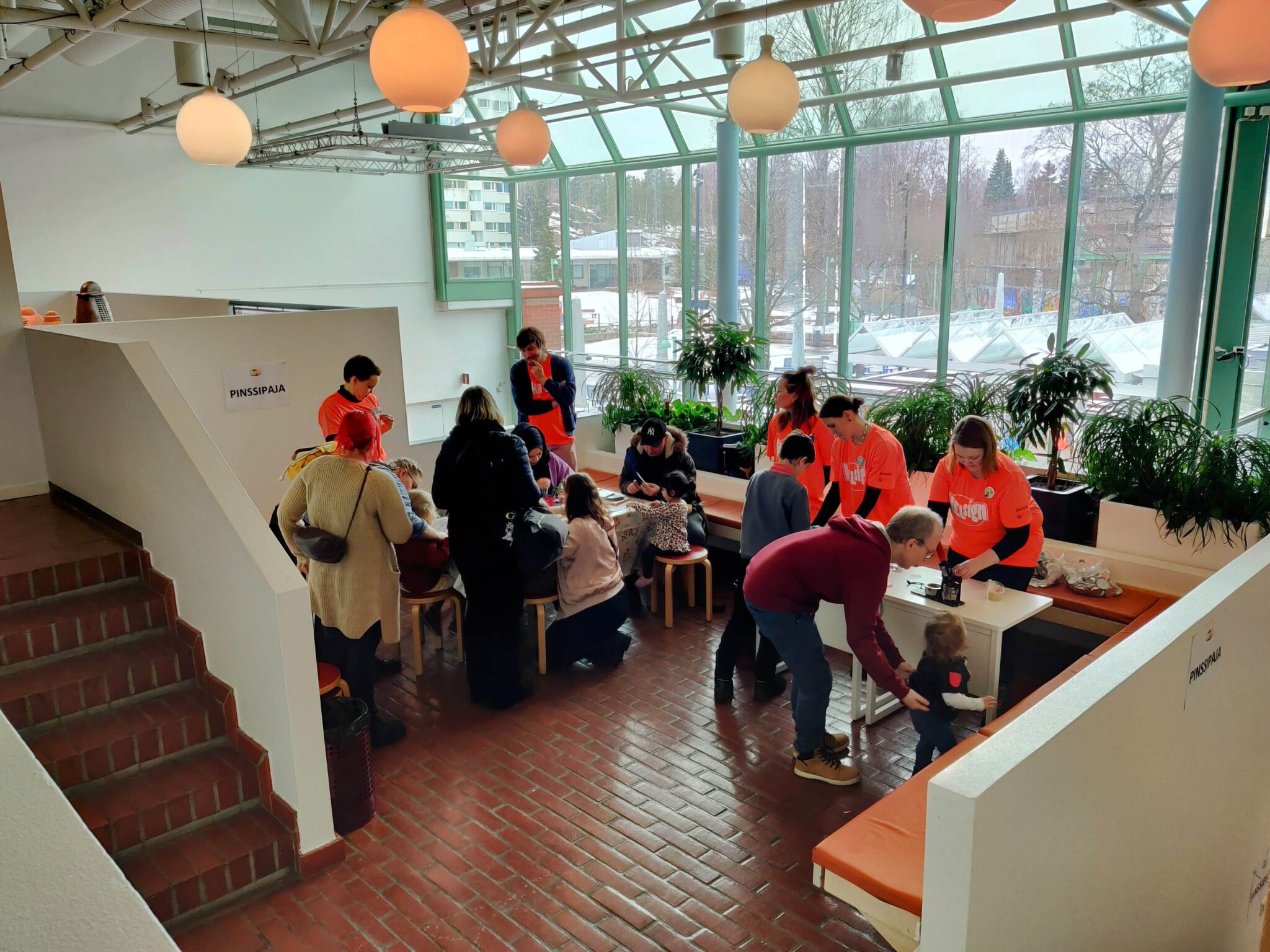 Pinssipajassa oransseihin Helsign-paitoihin pukeutuneet tulkkiopiskelijat auttavat perheitä ja lapsia tekemään itselleen rintaneulan valitsemastaan tai piirtämästään kuvasta.