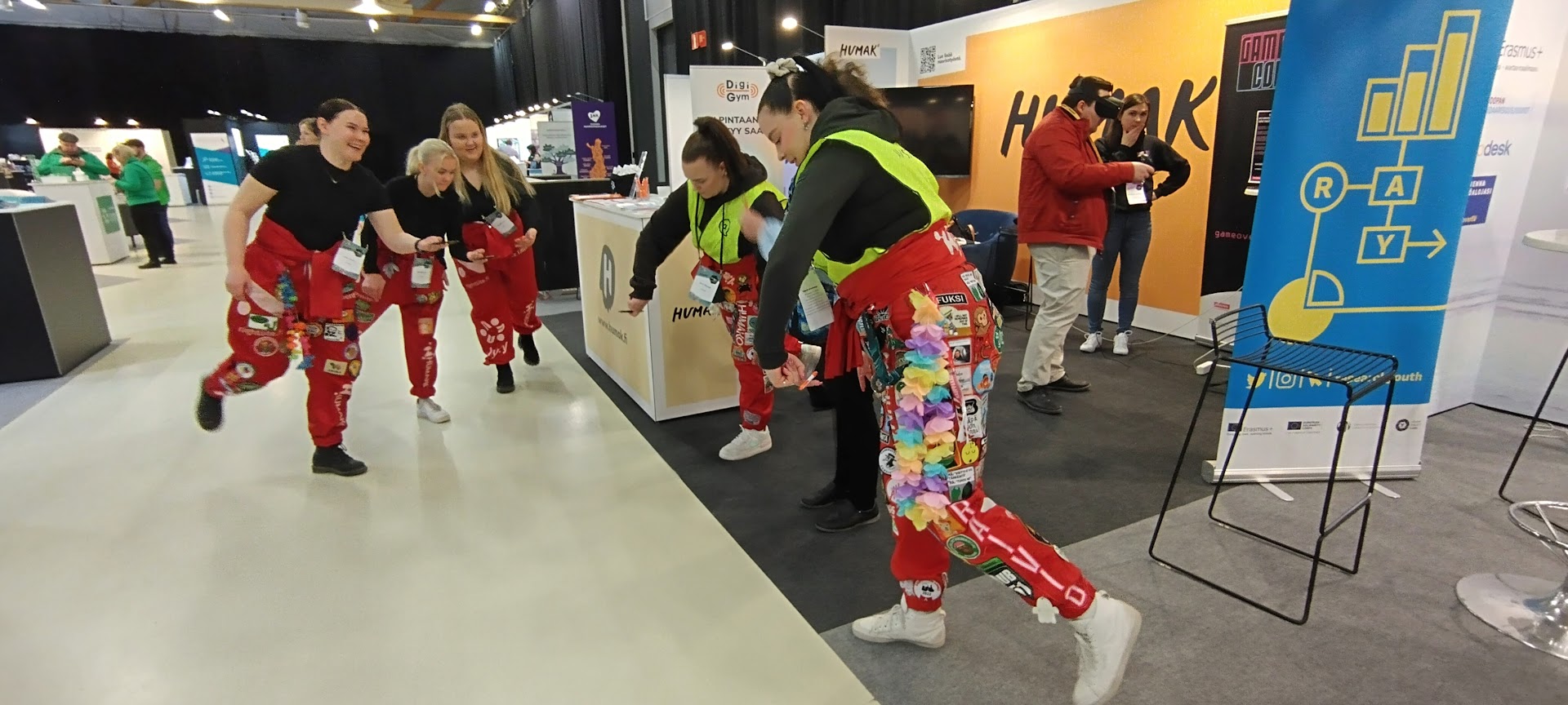 Messuosastolla opiskelijahaalareihin pukeutuneet naiset tasapainottelevat yhdellä jalalla.