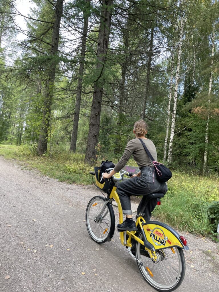 A young woman is riding a Helsinki city bike on a gravel trail in the forest.