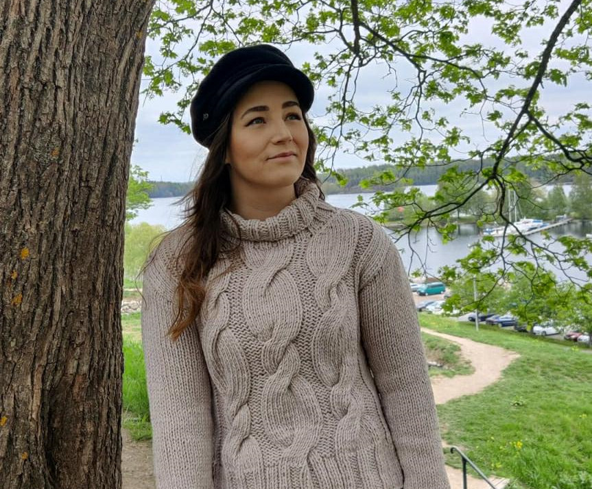 Kuvassa Iina, jolla on pitkät tumman ruskeat hiukset, neule ja hattu päässä.