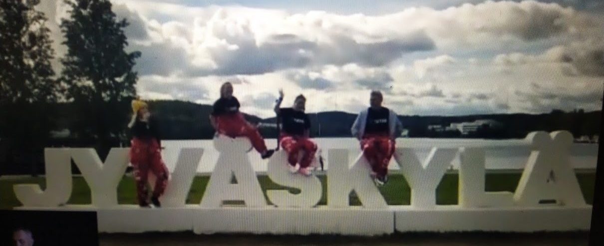 Videokaappauskuva Jyväskylä tutorit punaisissa haalareisa ja verryttelytakeissa, taustalla pilvinen taivas.