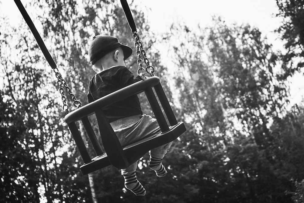 Mustavalkoisessa kuvassa pieni lapsi istuu keinussa, jossa asianmukainen turvakaari estää keinusta putoamisen.