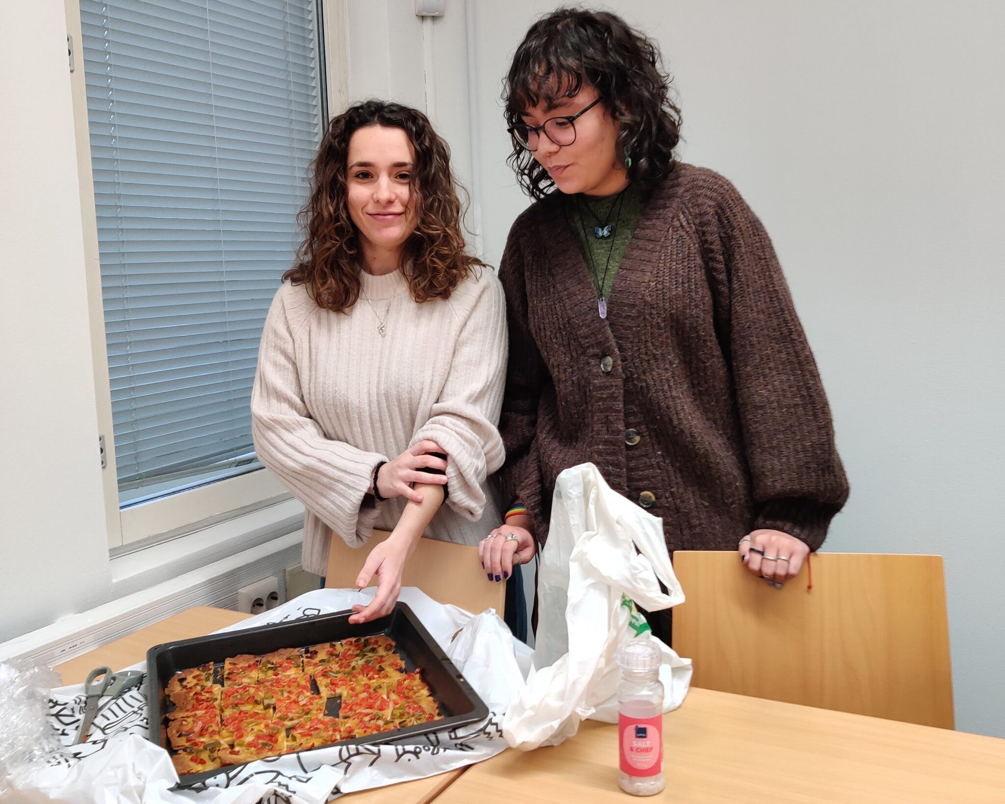 Addaia ja Graciel seisovat pöydän takana. Pöydällä on uunipellillä punainen leivonnainen.