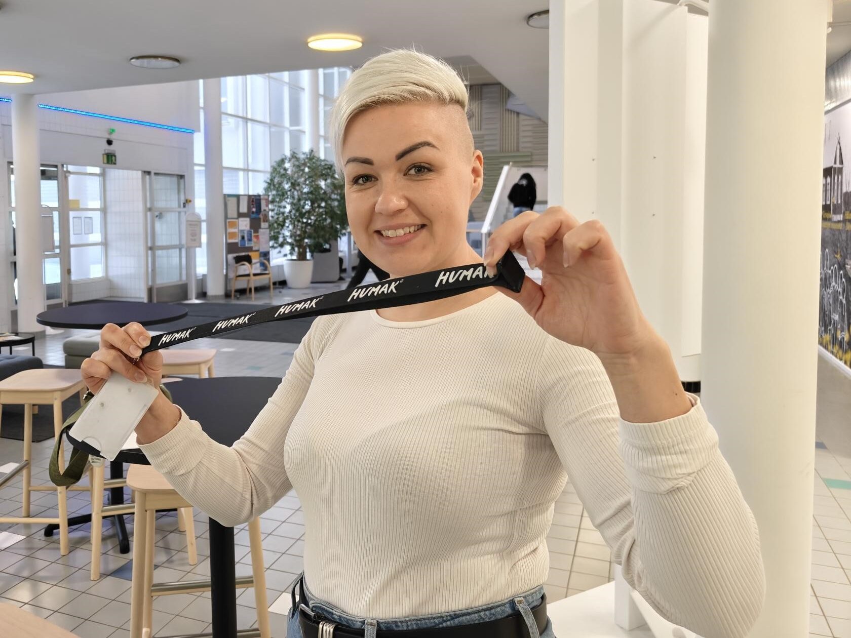 Kuvassa lyhythiuksinen vaalea nainen, aulatila, kädellä Humakin avainkaulanauha. 