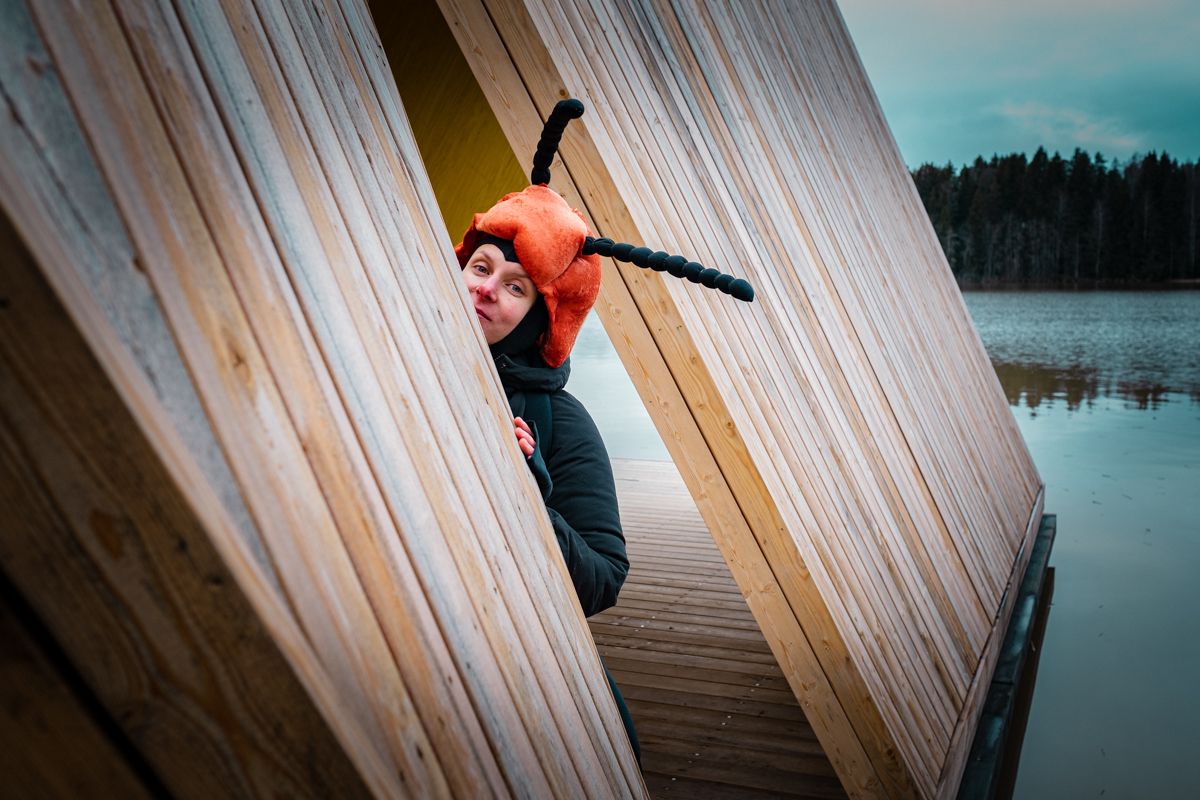 Kovakuoriaspuvussa oleva nainen kurkaa kohti kameraa laiturilla.