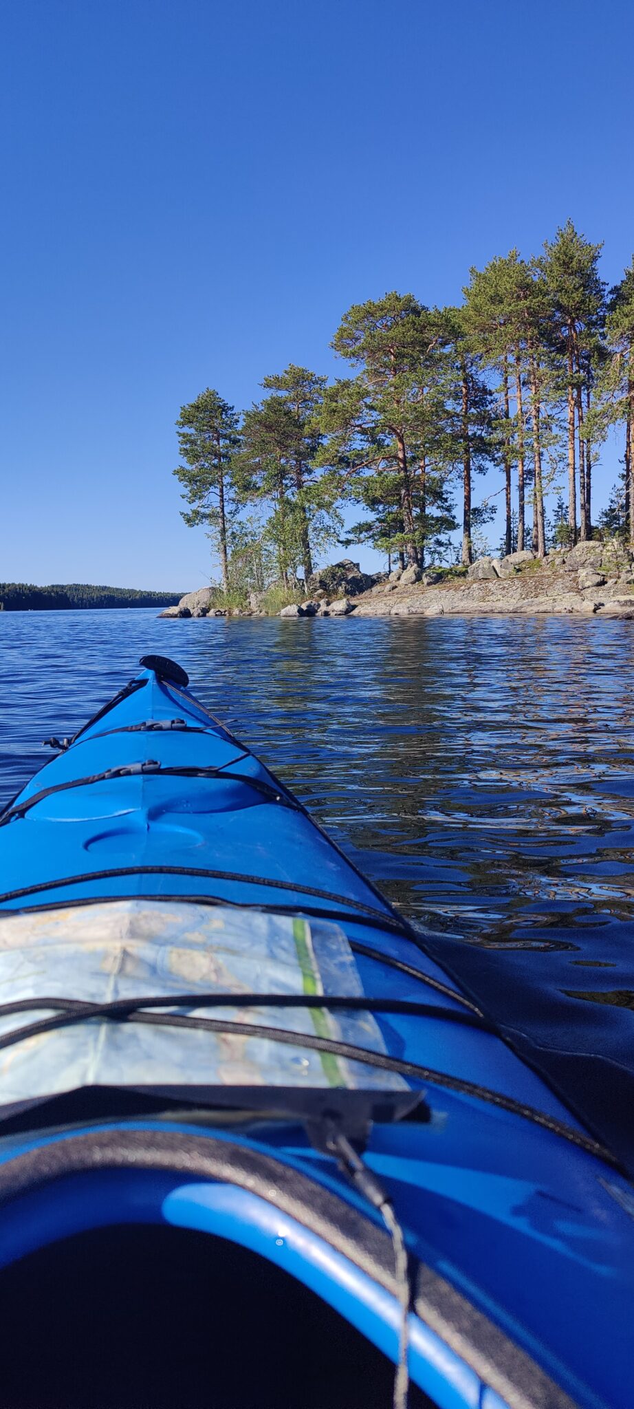 Melontaretki Päijänteellä. Kajakin keulan päällä on kartta, ja edessä näkyy aurinkoinen saari. Järven pinnassa on pieniä laineita.