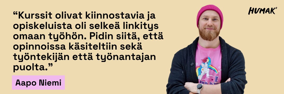 Mies seisoo kädet rennosti ristissä rinnan päällä. Hän hymyilee kameralle ja hänellä on päässä kirkkaan pinkki pipo. Mies näyttää iloiselta ja itsevarmalta.