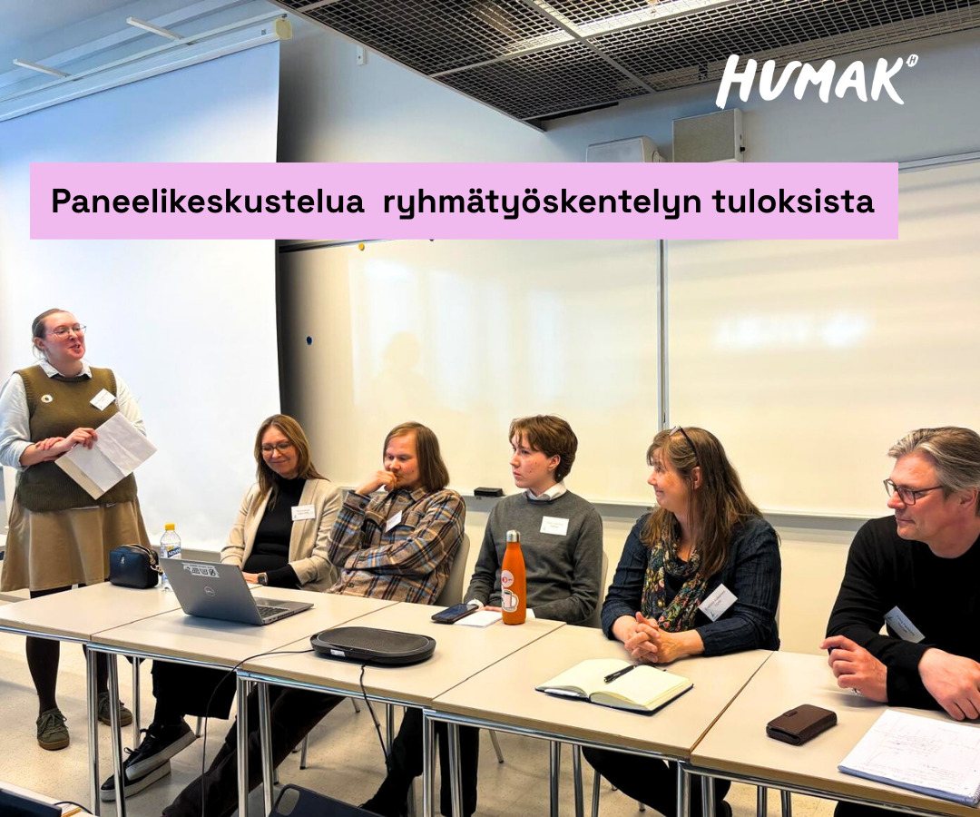 Paneelikeskustelun osallistujat istuvat pöytärivin ääressä. Keskustelun vetäjä seisoo pöydän vieressä ja kuuntelee osallistujien puheenvuoroja.