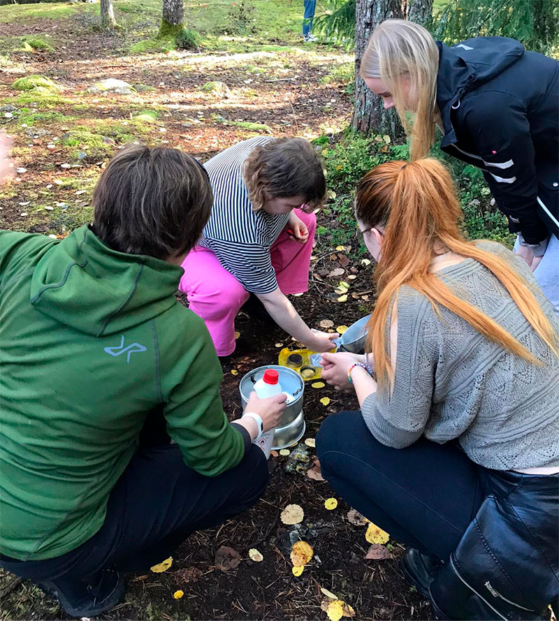 Neljä ihmistä kokoaa kyykyssä trangiaa metsässä.