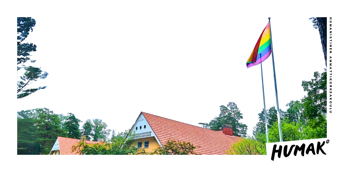 Kuvassa kohoaa punatiilinen katto kohti taivasta Takana näkyy metsää. Oikealla lipputangossa liehuu sateenkaarilippu. 