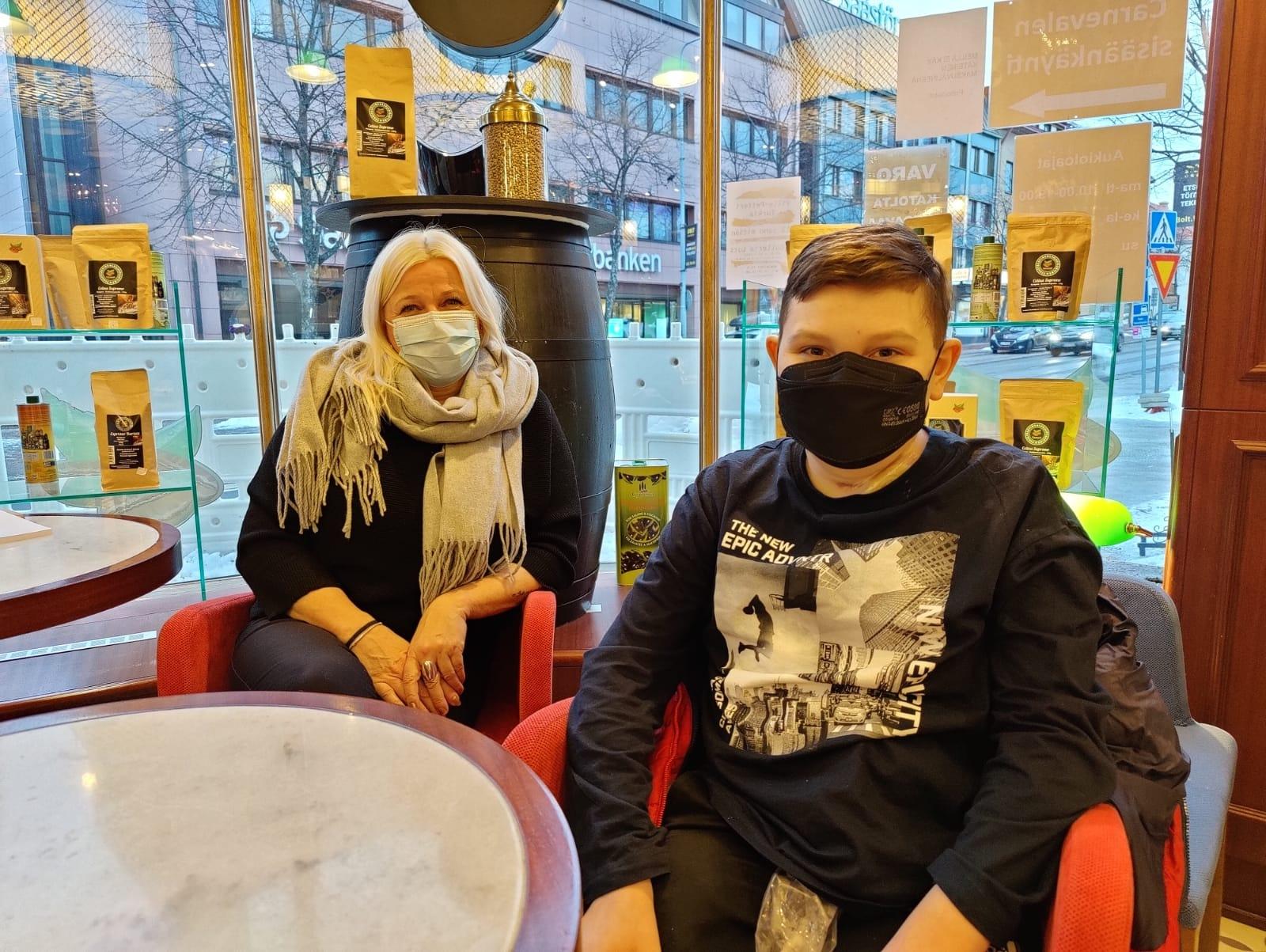 Vaaleahiuksinen nainen ja nuori poika istuvat kahvilassa.