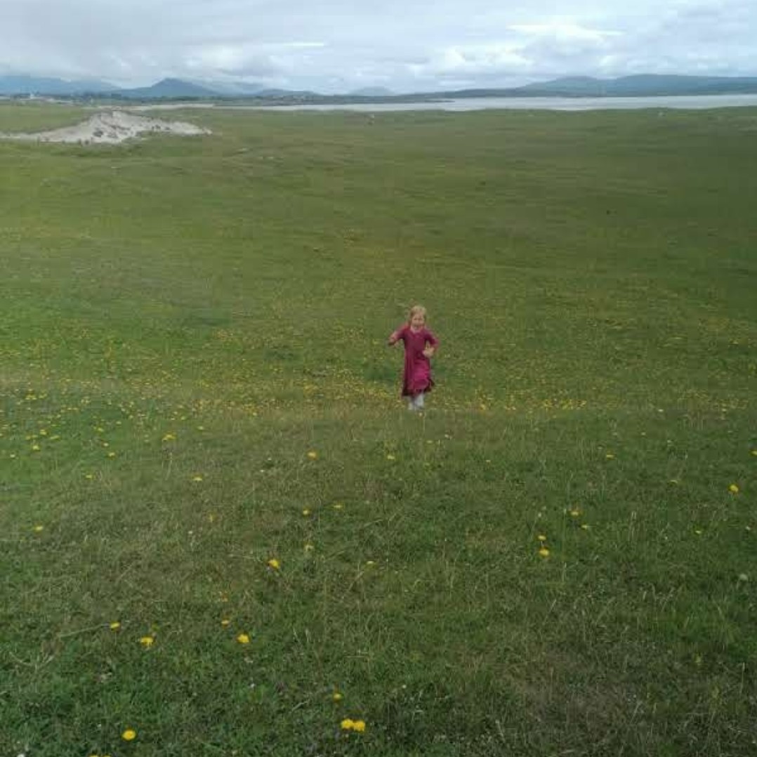 : tyttö juoksee viherniityllä pilvet taustanaan