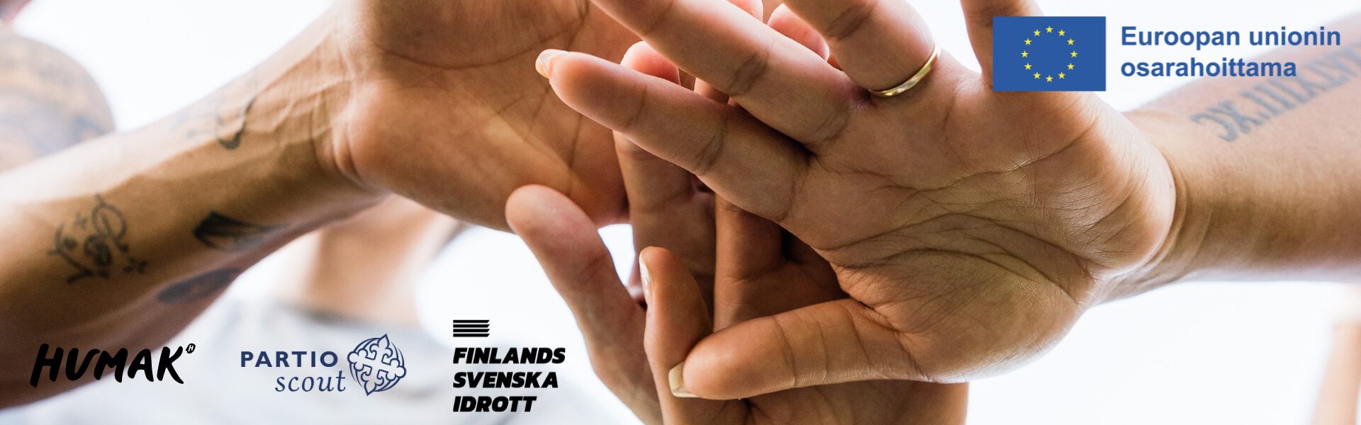 Kolme kättä koskettaa toisiaan yhdessäolon ja yhteistyön symbolina. Kuvassa näkyy tatuoituja käsivarsia ja sormuksia. Kuvan oikeassa yläkulmassa on EU:n lippu ja teksti 'Euroopan unionin osarahoittama'. Alareunassa ovat HUMAKin, Partio Scoutin sekä Finlands Svenska Idrottin logot.