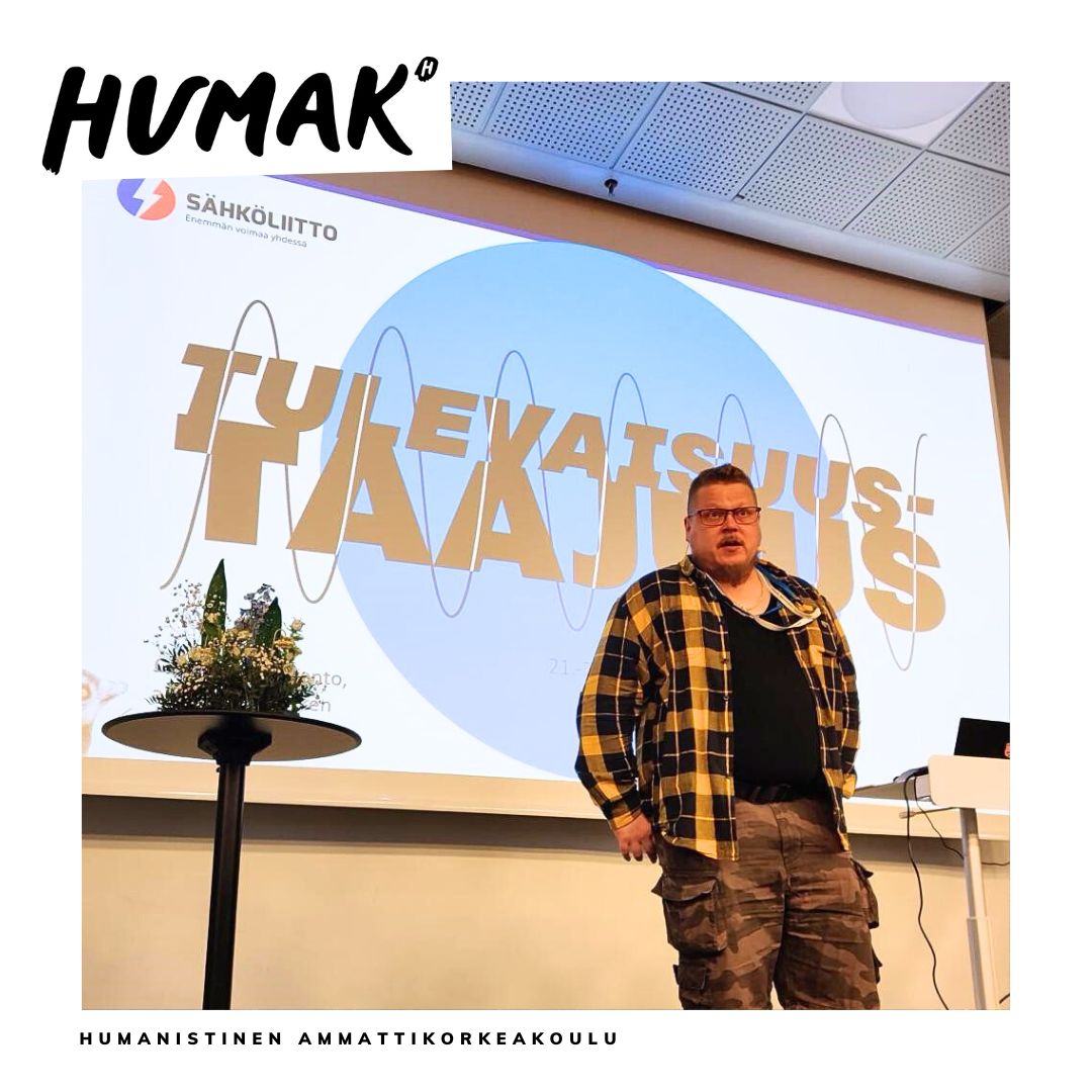 Valokuva seminaaritilaisuudesta, mies seisoo screenin edessä ja puhuu yleisölle. Screenissä lukee Tulevaisuustaajuus. 