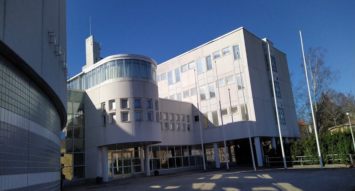 ValkeaTalo ulkoa, pihalla kaksi tyhjää lipputankoa, julkisivukuva.
