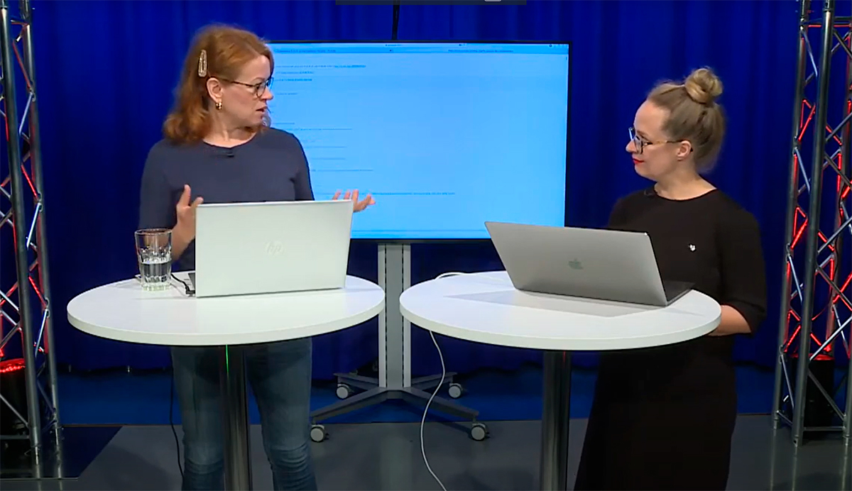 ALT: YLE:n asiantuntijat Tiina Klemettilä ja Marja Ollikainen seisovat pöydän ääressä ja keskustelevat vuorovaikutuksen mahdollisuuksista verkkotapahtumissa. Blogi teksti "Yleisön kohtaaminen".