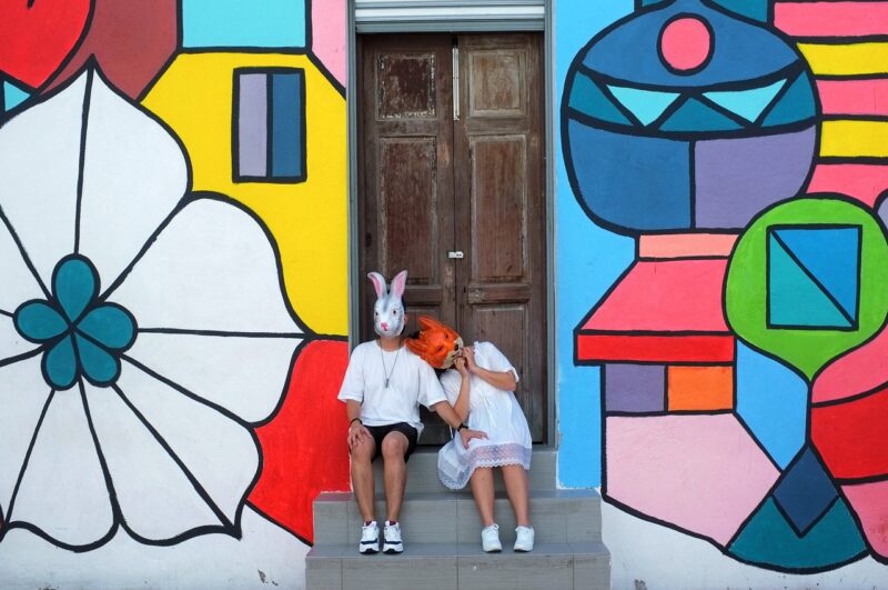 Kaksi henkilöä istuu värikkään muraalin edessä.