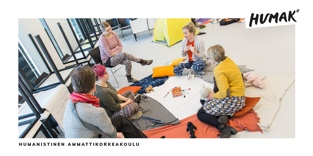 Viisi henkilöä istuu lattialla ja keskustelee.