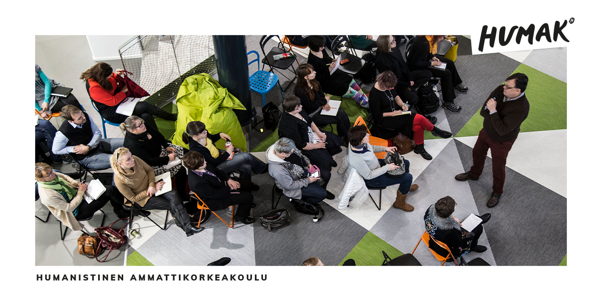 Ihmisiä istumassa penkeillä ja kuuntelemassa puhujaa.