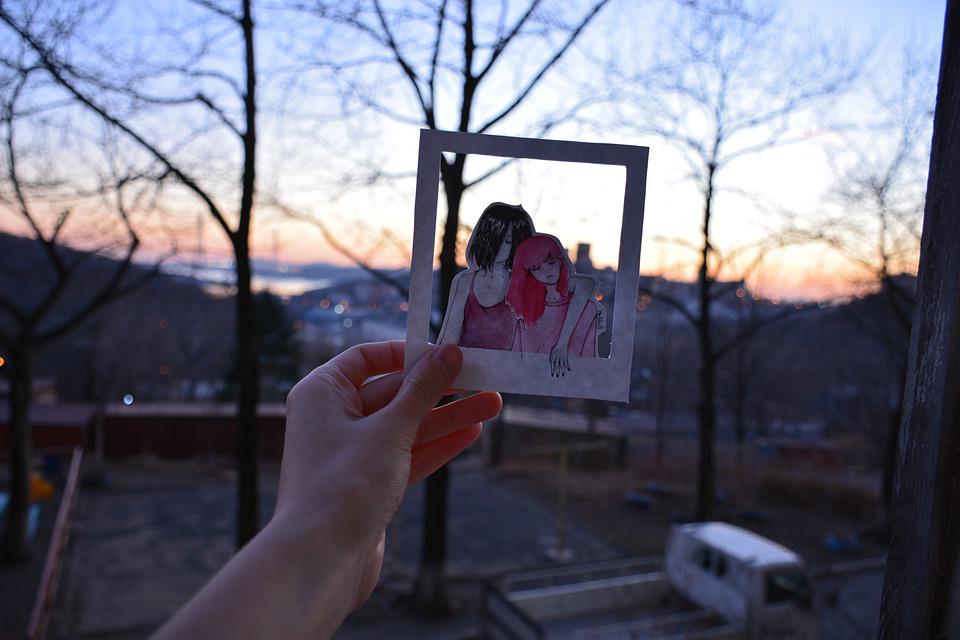 Henkilä pitää kädessään piirroskuvaa, jossa kaksi henkilöä nojaa toisiinsa. 