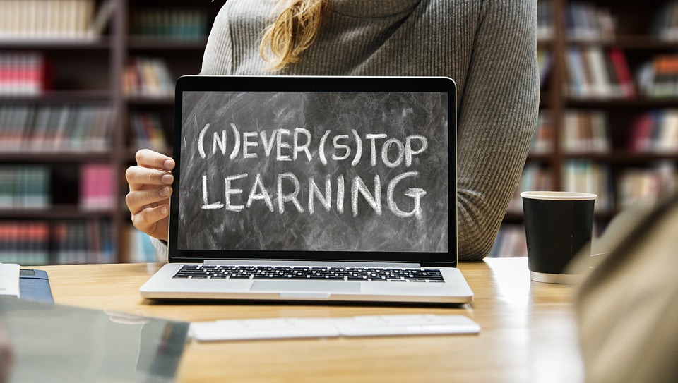 Henkilö istuu pöydän ääressä edessään katsojaan päin käännetty kannettava tietokone, jossa lukee sanat never stop learning.