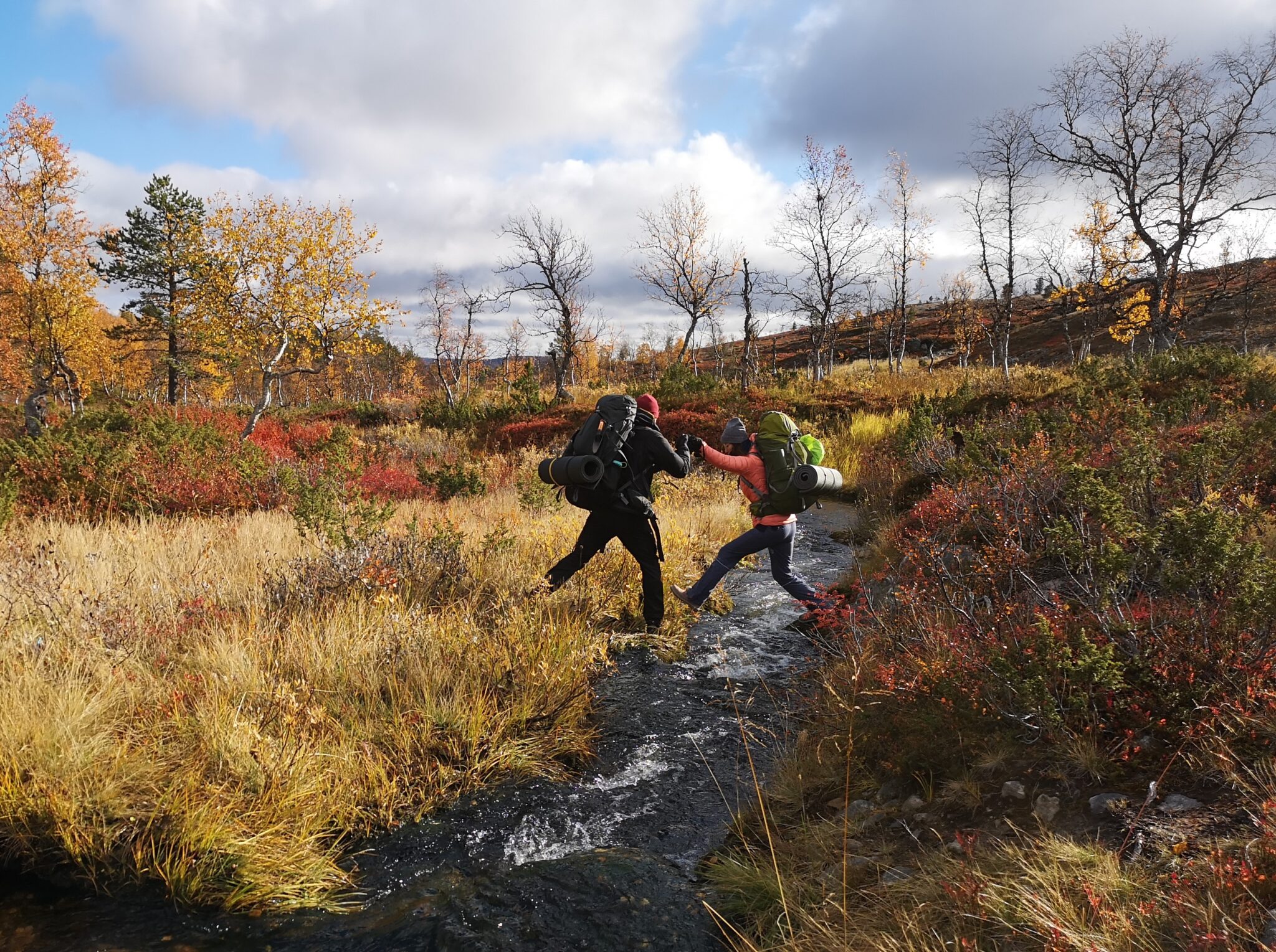 Kaksi nuorta ylittää puroa ja toinen auttaa.