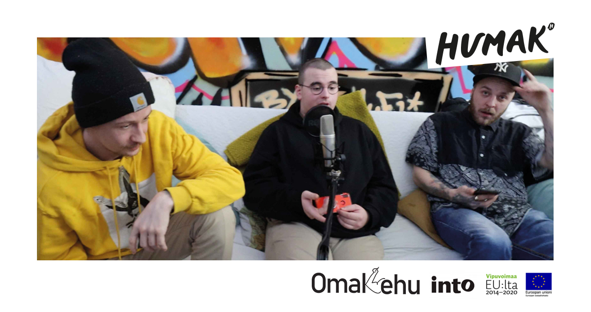 Kolme katumuotiin pukeutunutta miestä bäkkärin sohvalla.