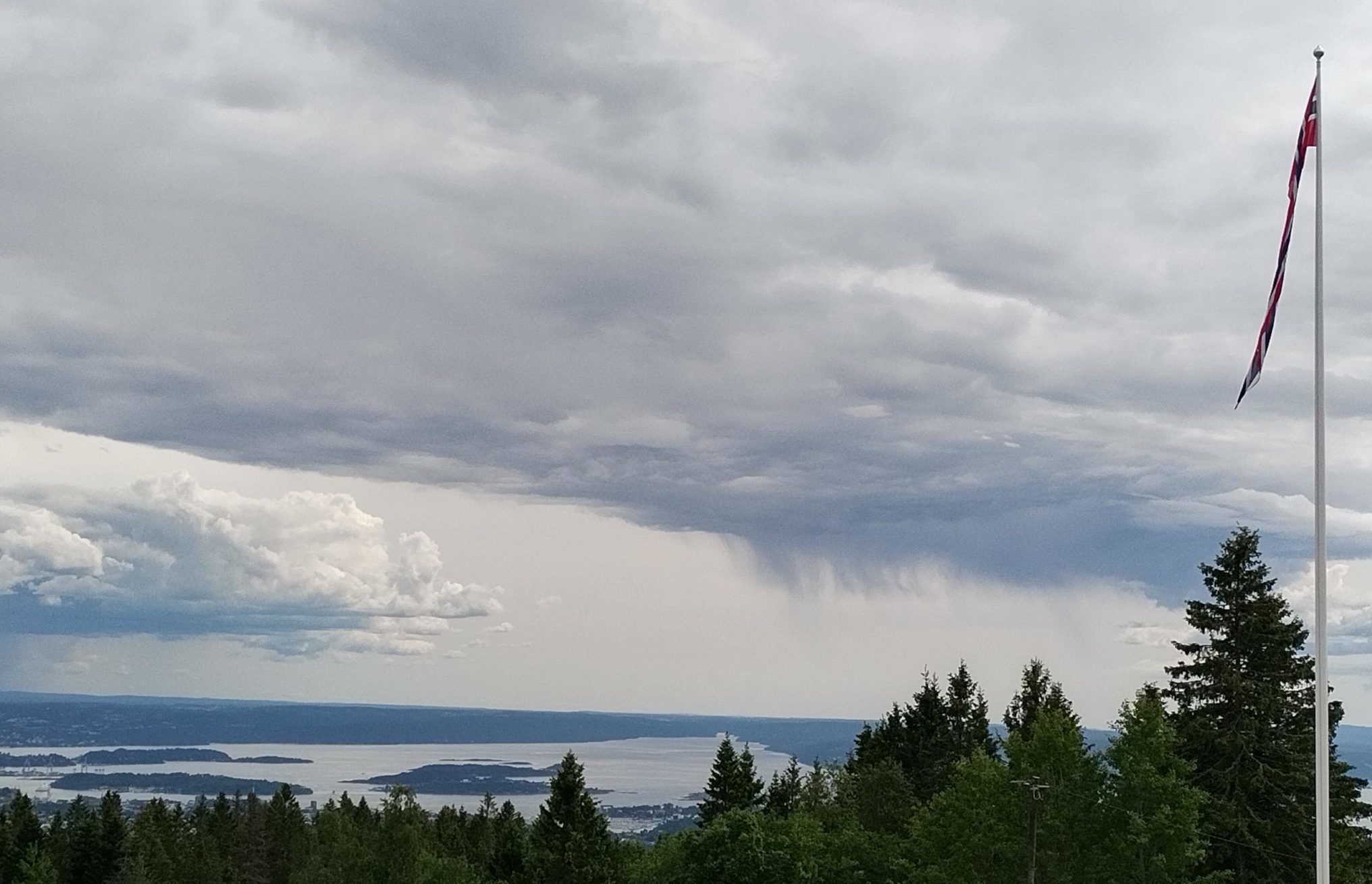 Maisema, jossa yläreunassa pilviä, näkymä merelle, etualalla puita ja metsää