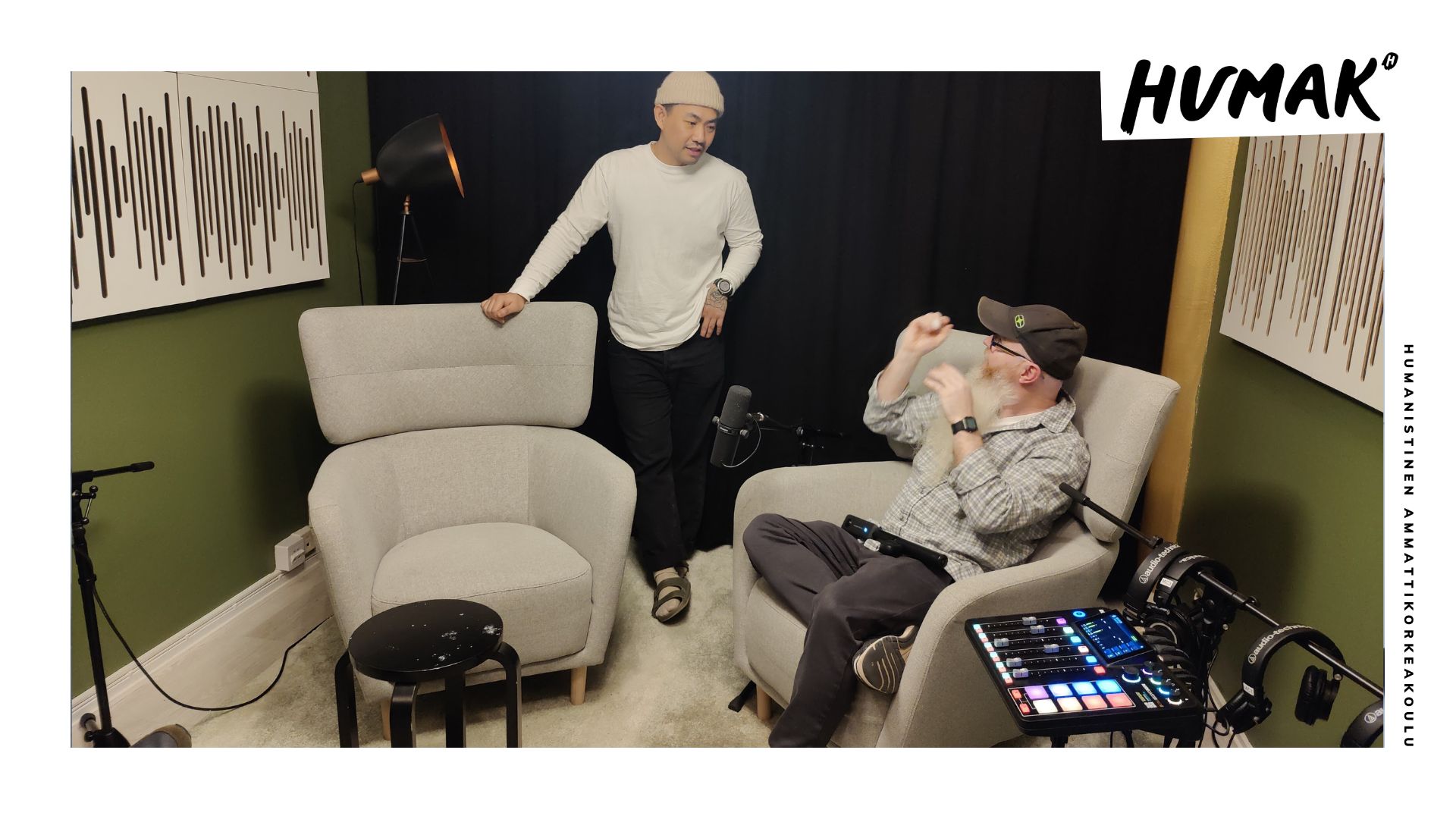 Kaksi henkilöä pienessä vaalean ja vihreän sävyihin sisustetussa huoneessa. Nuori mies seisoo ja nojaa pöytään, vanhempi mies istuu äänisuunnitteluun liittyvän laitteiston vieressä.