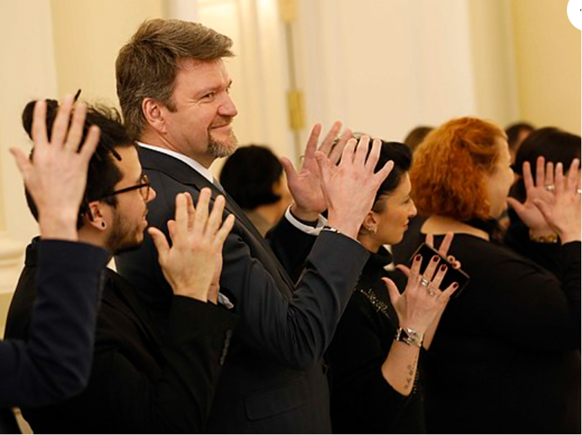 ryhmä tummiin pukeutuneita ihmisiä pitävät avoimia kämmeniä ylhäällä ja näyttävät iloisilta