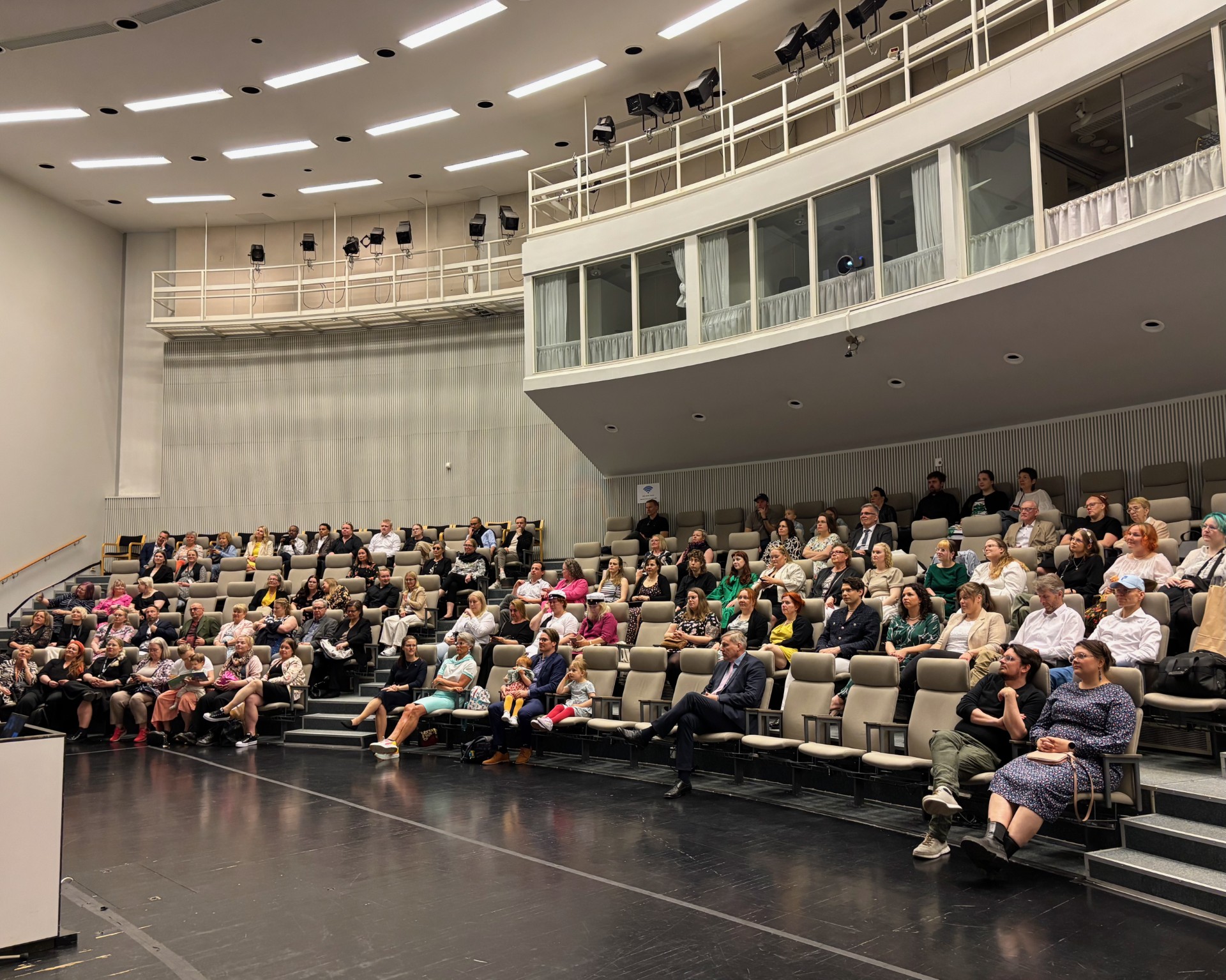 Yleisö istuu puolikaaren muotoisessa auditoriossa.