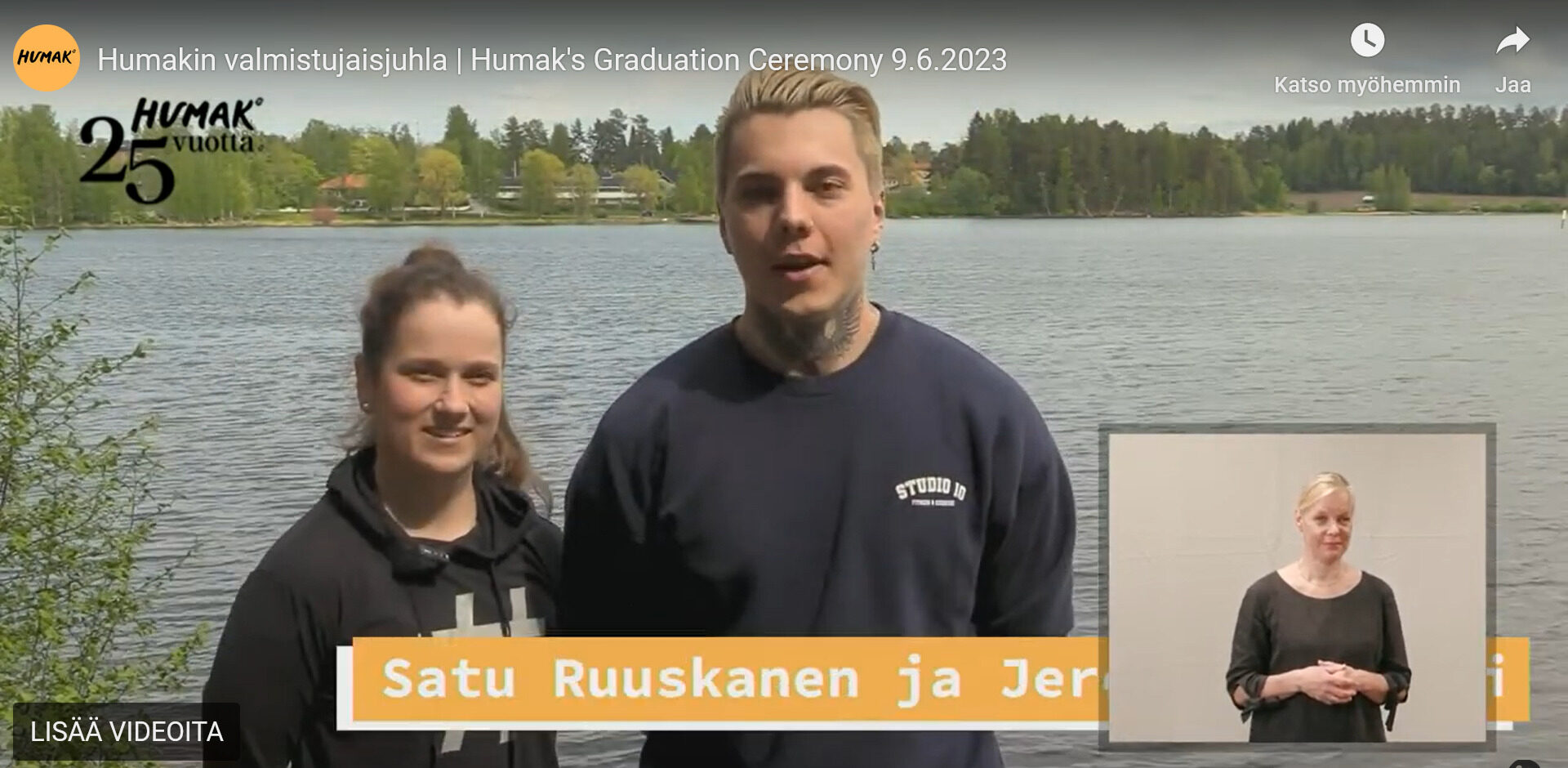 Kuvakaappauskuvassa nuori nainen ja mies seisovat järvimaisemisssa pitämässä puhetta Humaki valmistujaisjuhlan videolähetyksessä. 