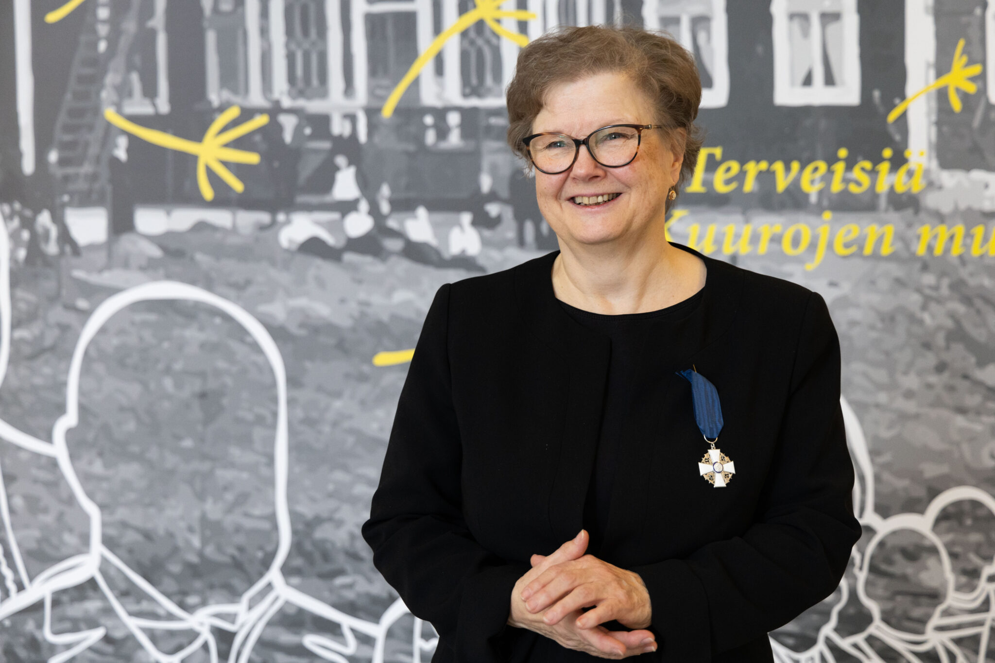 Tutkija Päivi Raino hymyilee Valkean talon aulassa kunniamerkki rinnassaan.