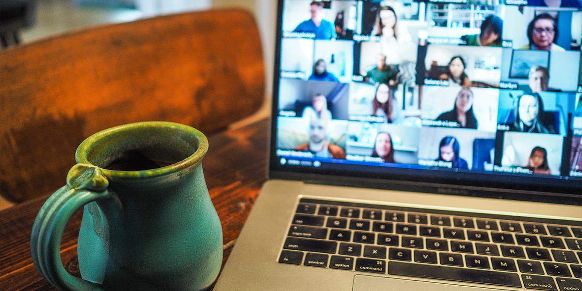 Pöydällä vihreä kahvikuppi ja vieressä tietokone, jonka ruudulla paljon webinaariosallistujia.