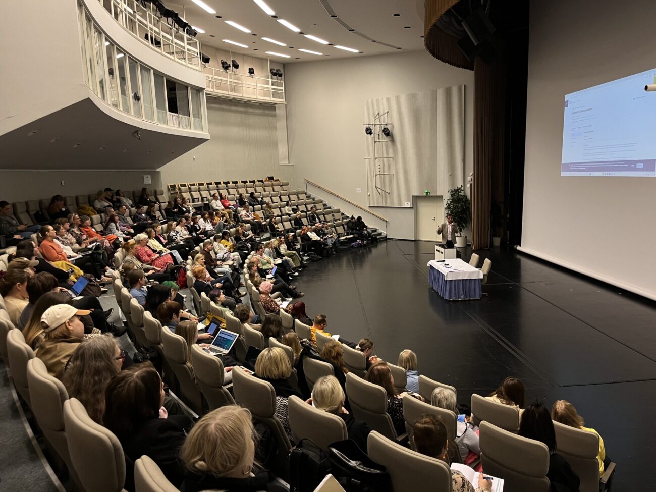 Paljon ihmisiä auditoriossa kuuntelemassa esitystä.