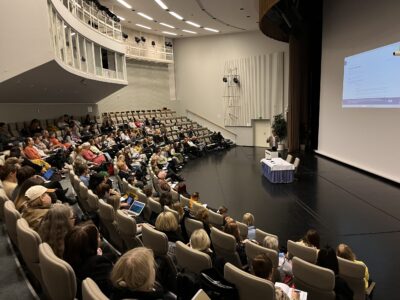 Paljon ihmisiä auditoriossa kuuntelemassa esitystä.