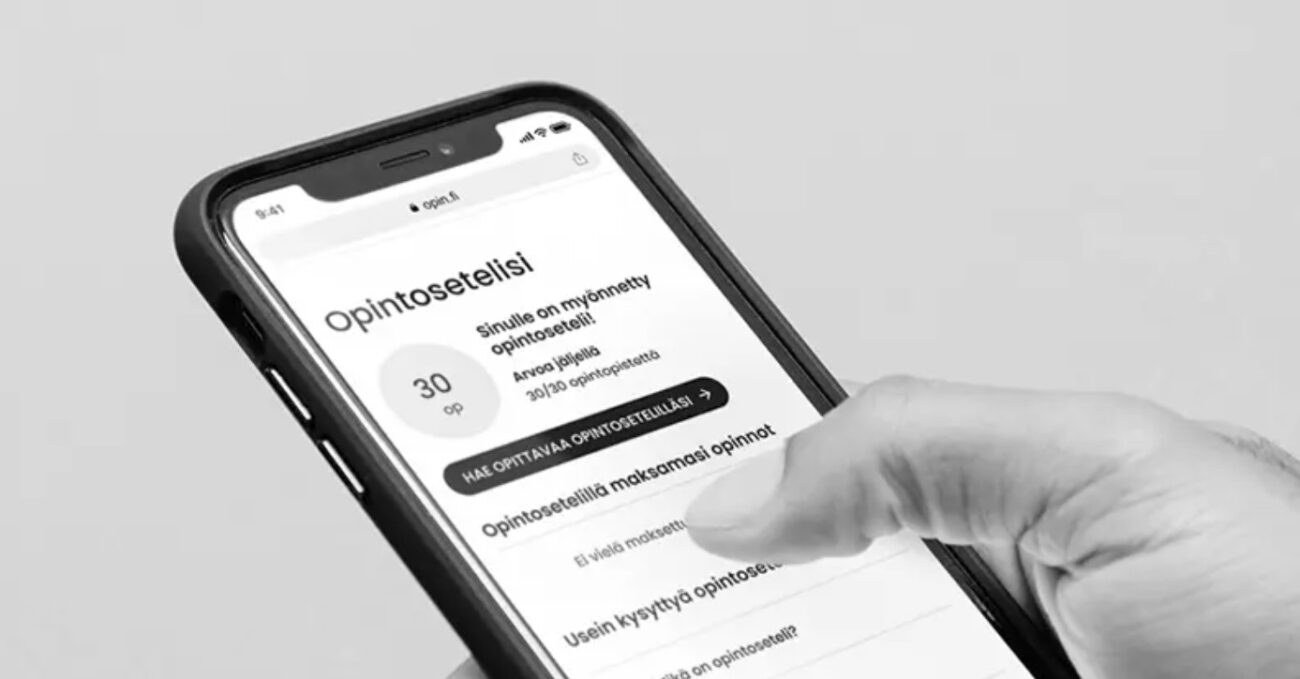 Käden pitelemä älypuhelin pystyasennossa, näytöllä suomenkielinen Opintoseteli-sovellus jossa näkyy otsikko Opintoseteli ja valintoja, sormi koskettaa näyttöä.