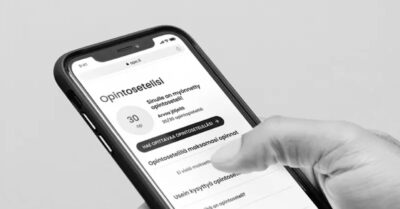Käden pitelemä älypuhelin pystyasennossa, näytöllä suomenkielinen Opintoseteli-sovellus jossa näkyy otsikko Opintoseteli ja valintoja, sormi koskettaa näyttöä.