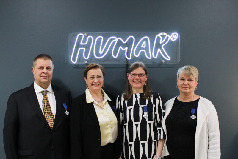 Kuvassa neljä henkilöä, vasemmalla mies, sitten kolme naista, taustalla Humak-valokyltti, ryhmä seisoo seinän edessä. 