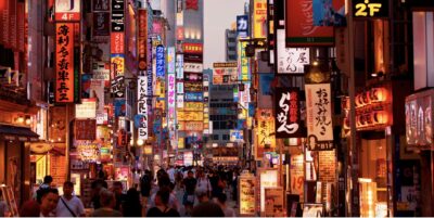 Vilkas japanilainen iltakatu, jossa ravintoloiden ja kauppojen värikkäiden neonkylttien ja paperilyhtyjen alla kulkee väkijoukko.