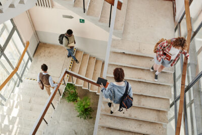 Overview of teenage students going up and down staircase in corridor while leaving for home or another university building