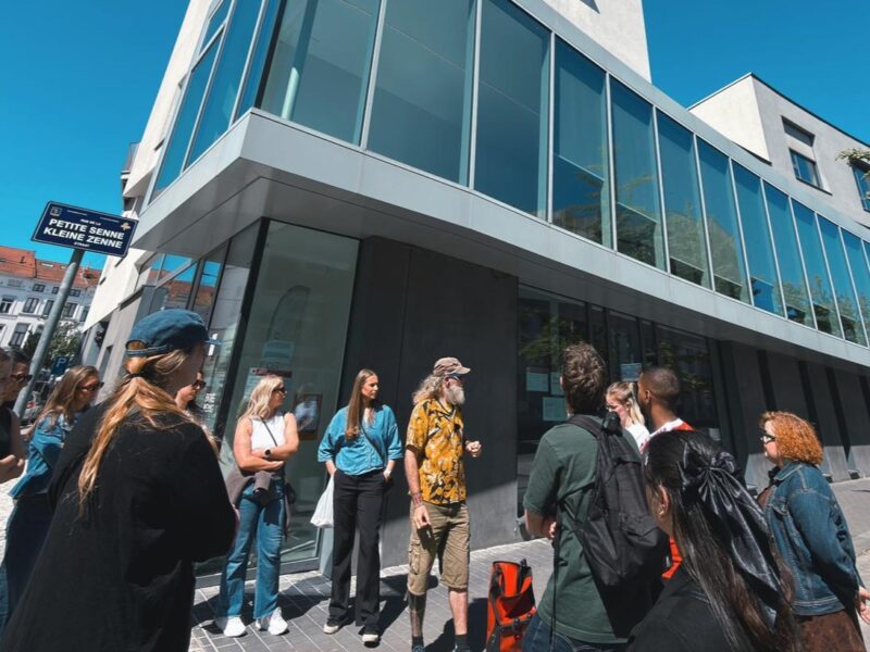 Opiskelija ryhmä kuuntelee oppaan esittelyä modernin rakennuksen edustalla.