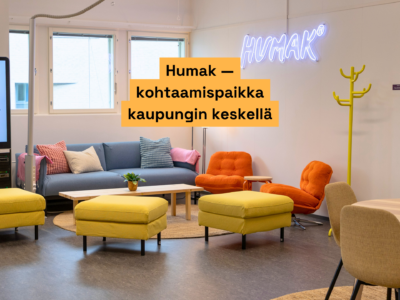 Viihtyisä oleskelutila, jossa vaaleansininen sohva koristetyynyineen, oranssit nojatuolit, keltaiset rahi­ryhmät ja pikkupöytä ruukkukasvilla, seinällä sininen neonkyltti "HUMAK" ja oranssi laatikko, jossa teksti "Humak – kohtaamispaikka kaupungin keskellä".