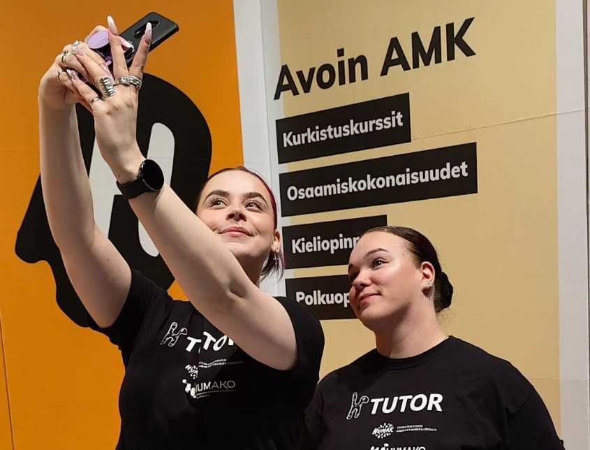 Messuilla työskentelevät korkeakouluopiskelijat poseeraavat kameralle iloisesti hymyillen.