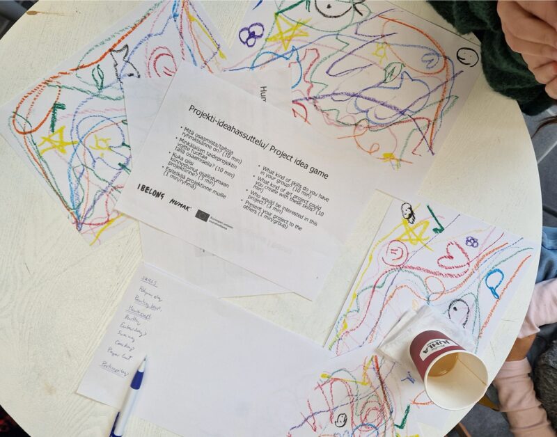A round table viewed from above, with drawings, notes, a coffee cup, and a piece of paper containing questions to support the project planning.